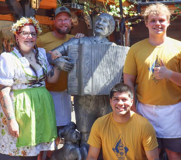 München Haus team standing by the statue in the beer garden.